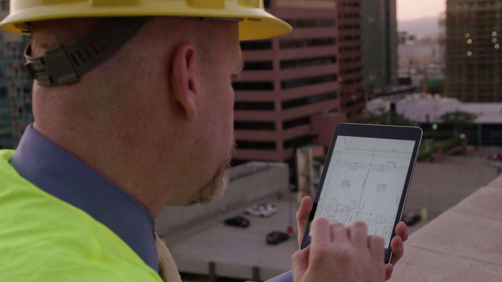 Bouwvakker op dak controleert bouwplan op tablet met stadsgezicht op achtergrond