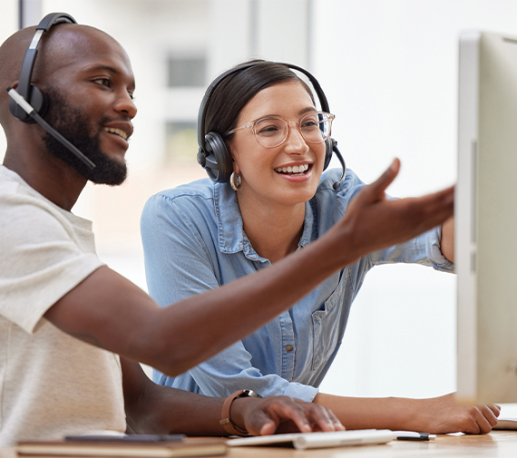 Twee collega's met headsets werken samen aan computer en glimlachen tijdens videoconferentie